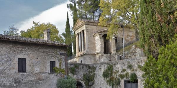  The Tempietto del Clitunno, a Lombard-era temple-shaped building with columns and a pediment, nestled in the greenery of the Umbrian countryside 